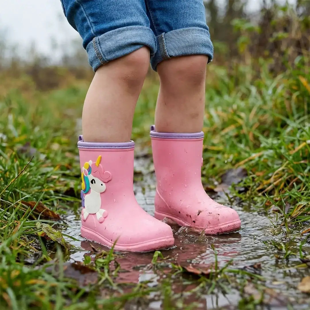 Niña de pie en un charco usando botas de agua rosadas.
