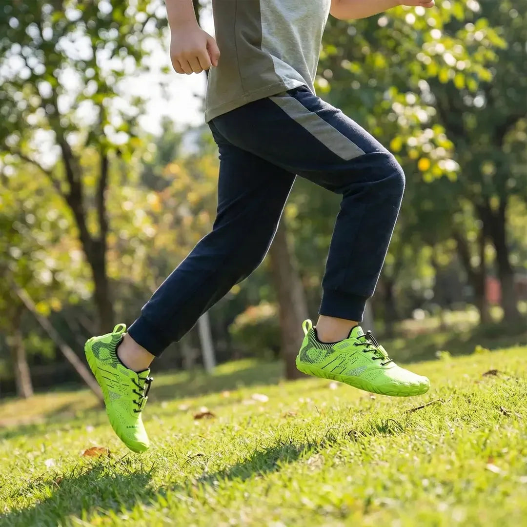 Niño corriendo en parque usando zapatillas barefoot Saguaro Kids verde flúor.