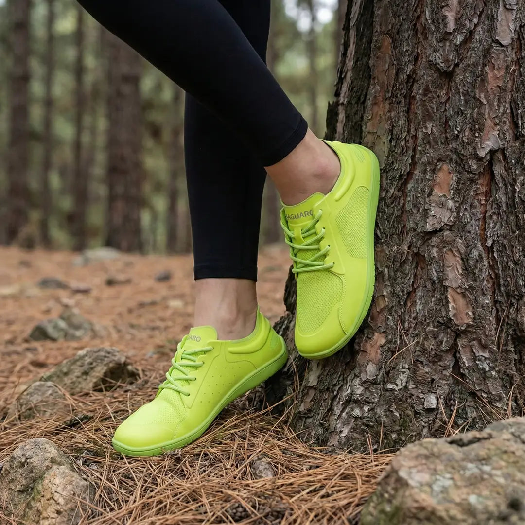 Persona apoyada en un tronco usando zapatillas barefoot mujer Saguaro Wish II verdes.
